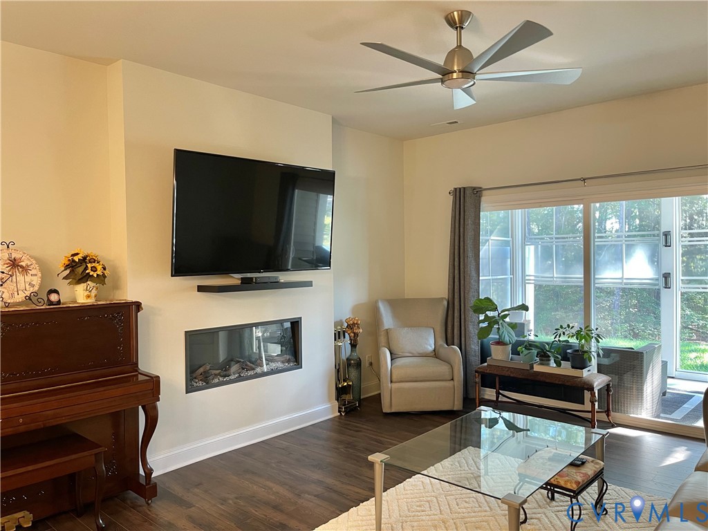 Wood-finish flooring, ceiling fan with brushed nickel finish, mounted television, linear electric fireplace, and sliding glass door leading to the exterior