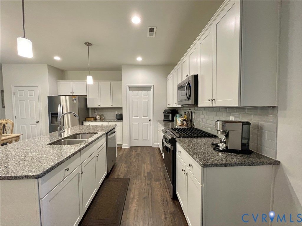 Kitchen featuring an expansive island with a double basin sink, stainless steel appliances, white shaker-style cabinetry, granite countertops, and a subway tile backsplash