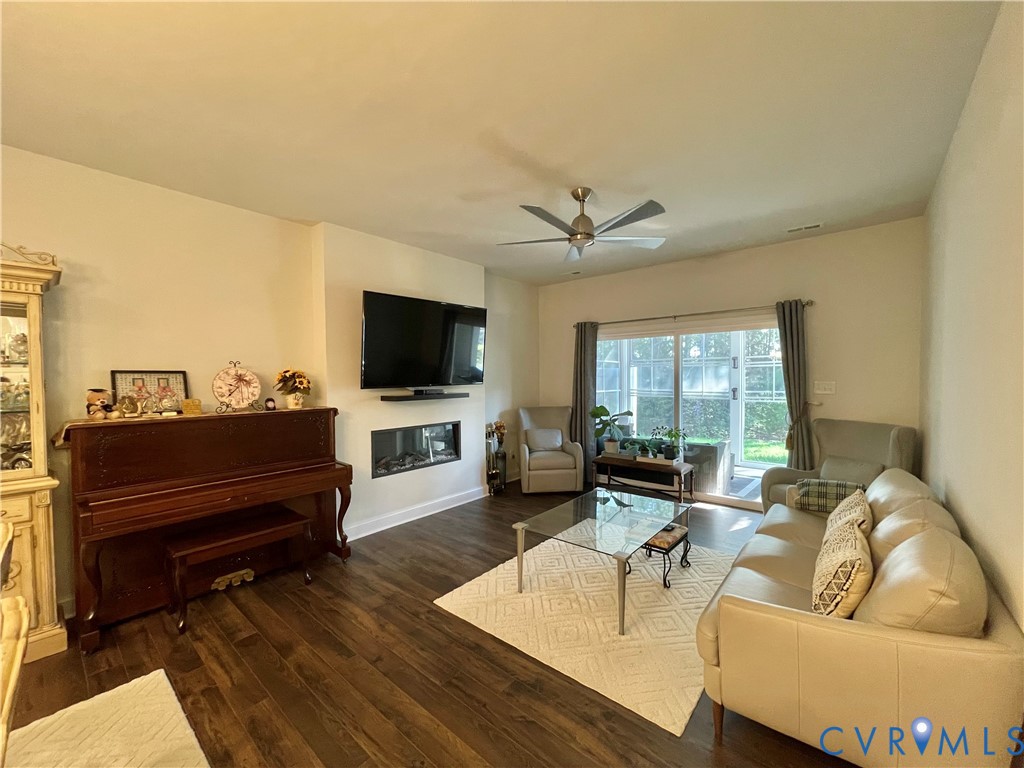 Wood-finish flooring throughout, featuring a linear fireplace, wall-mounted television, and a ceiling fan