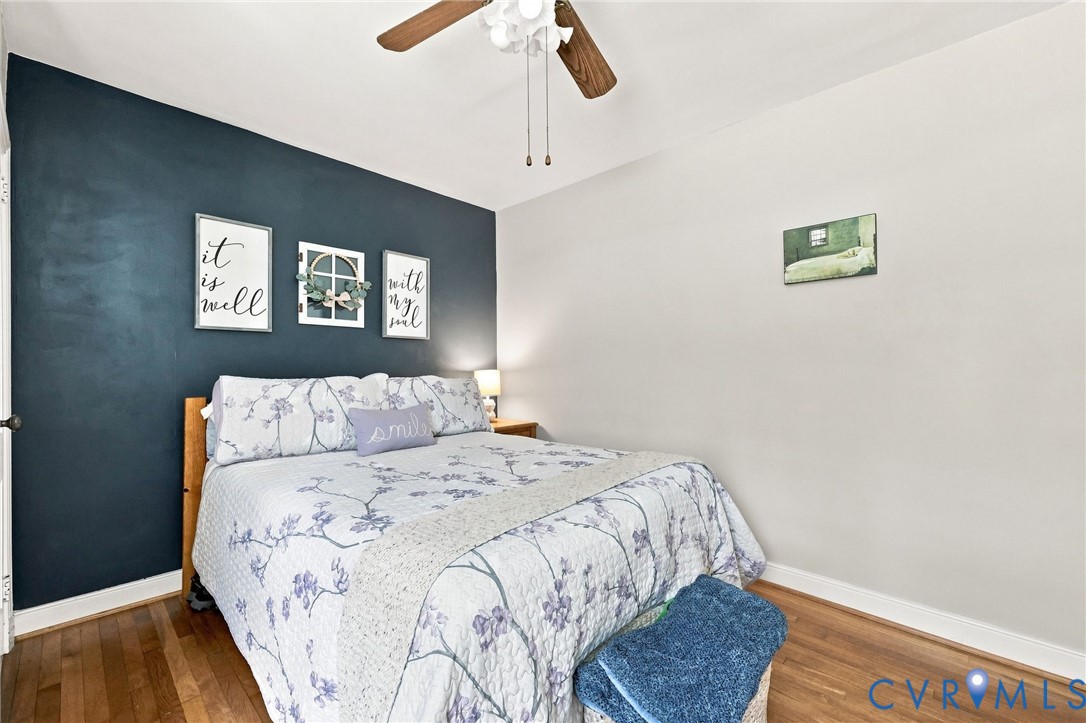 Hardwood flooring, ceiling fan with light fixture, and a dark accent wall
