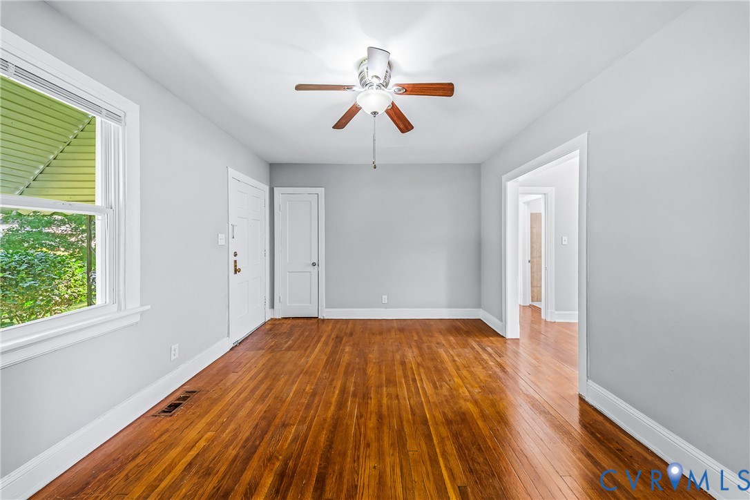 Refinished wood flooring, light gray wall tones, ceiling fan with wood-finish blades, white trim, and abundant natural light