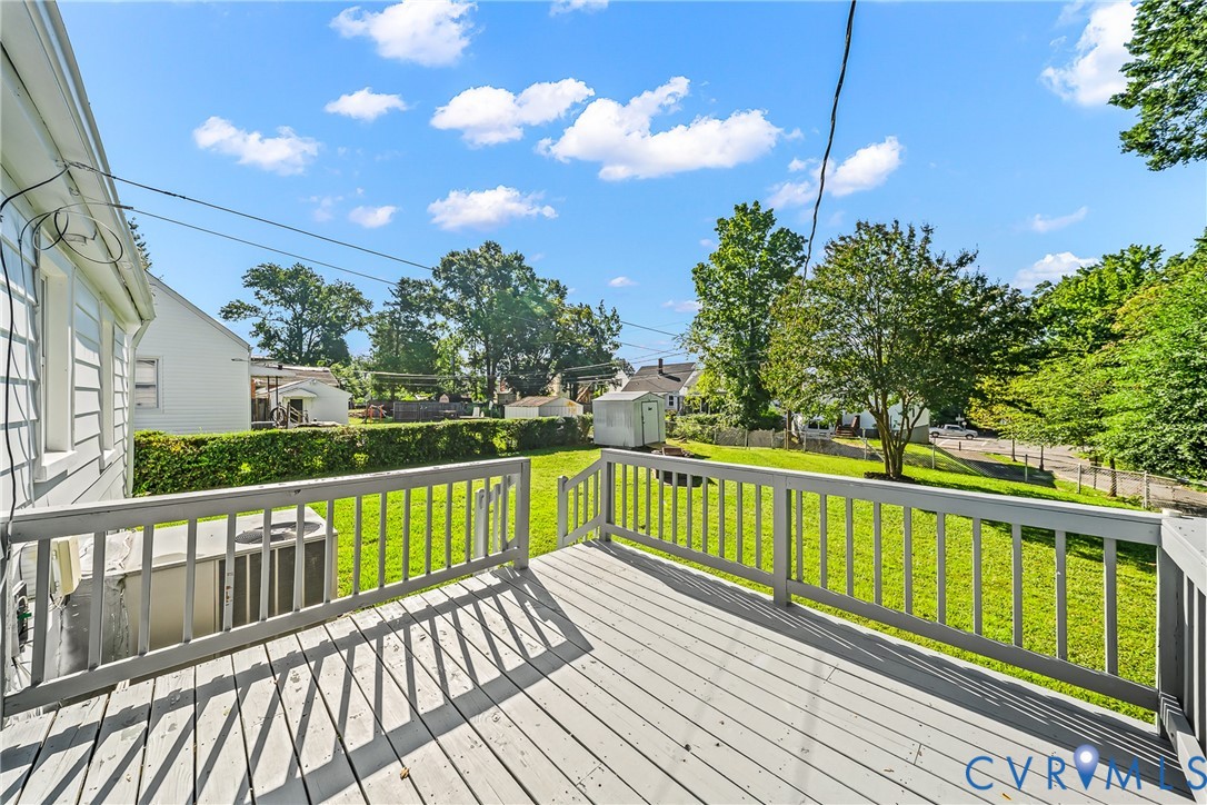 Outdoor deck with painted railing and wood-finish flooring overlooking a manicured lawn
