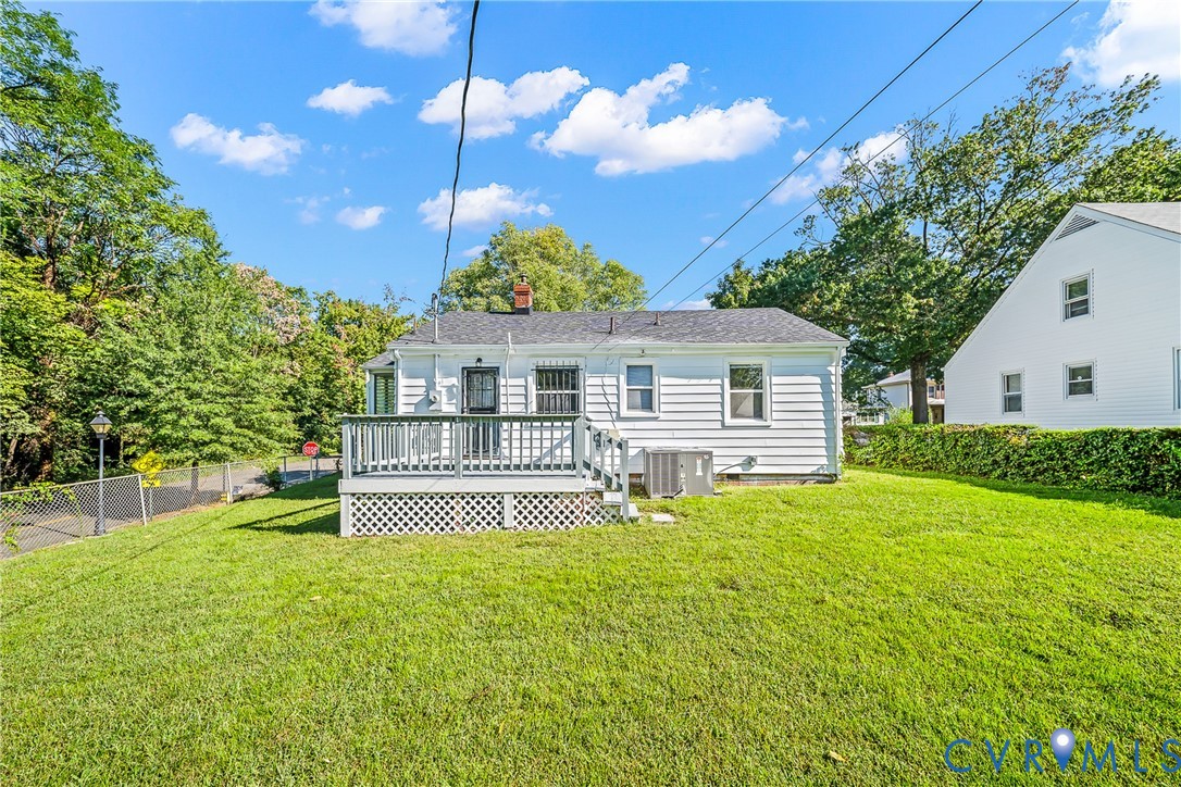Rear exterior showcasing white siding, a raised deck with dark railings, a lattice skirt, and a manicured lawn