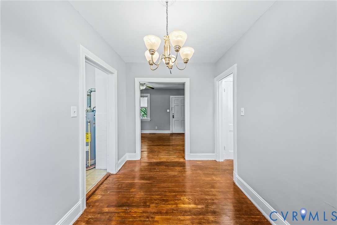 Hallway featuring wood-finish flooring, light gray walls, white trim, and a bronze-finish chandelier with frosted glass shades