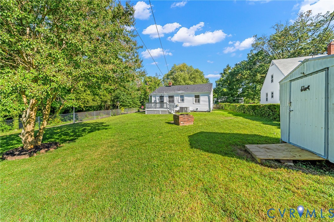 Expansive grassy yard featuring mature trees, a detached storage shed, and a brick fire pit