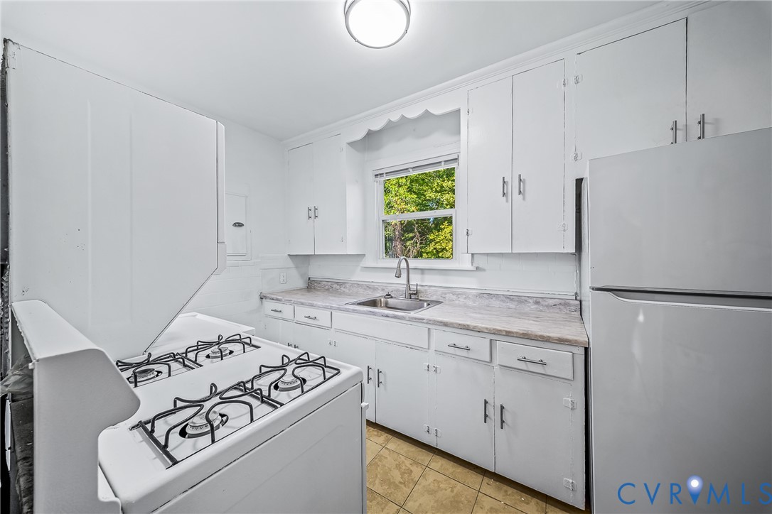 Kitchen featuring white cabinetry, a sink with a gooseneck faucet, light-toned countertops, and a gas range