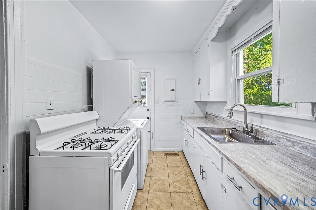 White cabinetry, wood-finish countertops, stainless steel sink, tile flooring, and a gas range