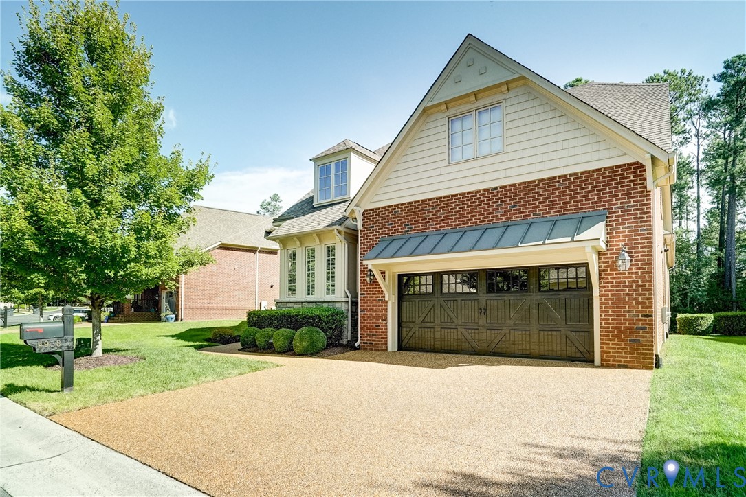 Brick exterior with siding accents, attached garage with decorative doors, dormer window, bay window, and manicured landscaping
