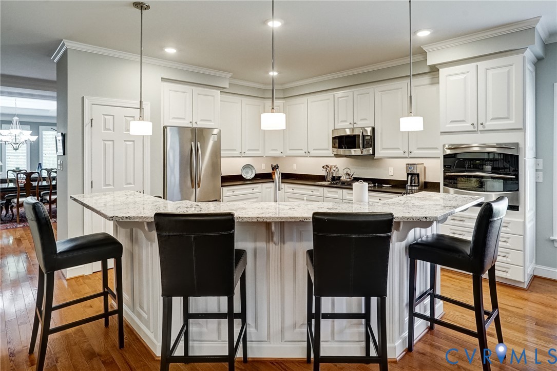 Kitchen featuring white cabinetry, stainless steel appliances, a multi-level island with seating, and wood-finish flooring