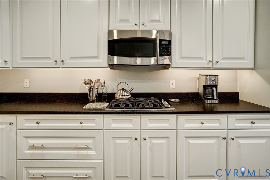 White cabinetry with panel doors, dark countertops, a built-in stainless steel microwave, and an integrated gas cooktop