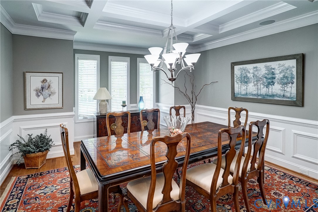 Coffered ceiling with a suspended chandelier, wood-finish flooring, wainscoting, and multiple windows