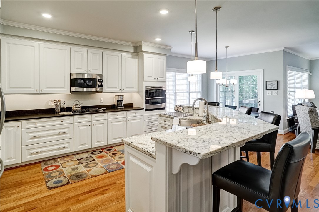 White cabinetry, stainless steel appliances, granite countertops, hardwood flooring, and pendant lighting