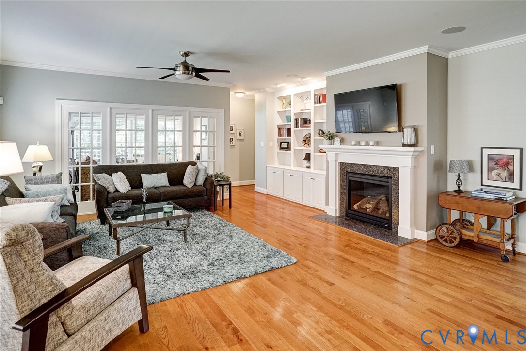 Hardwood flooring throughout, a ceiling fan, built-in shelving, a fireplace with a stone surround, and French doors