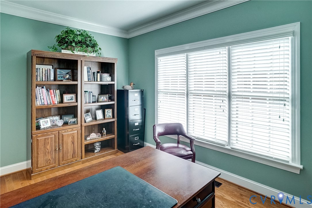 Wood-finish flooring, built-in shelving, crown molding, and large windows with blinds