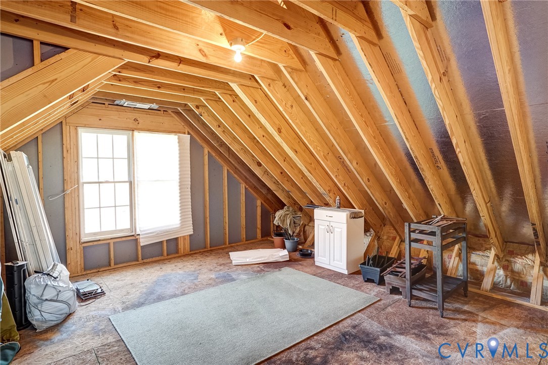Exposed wood beam ceiling, attic space, dual-pane window, built-in cabinetry, and wood subflooring