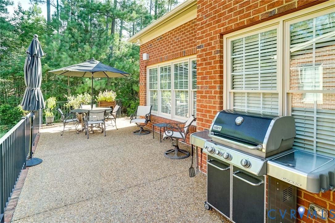 Brick exterior with multiple windows, exposed aggregate patio, and metal railing