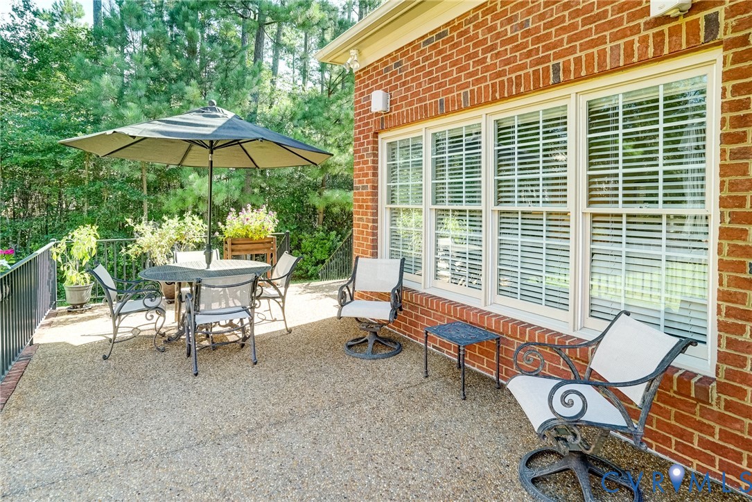 Brick exterior with a textured patio surface, black metal railing, and multiple windows with blinds