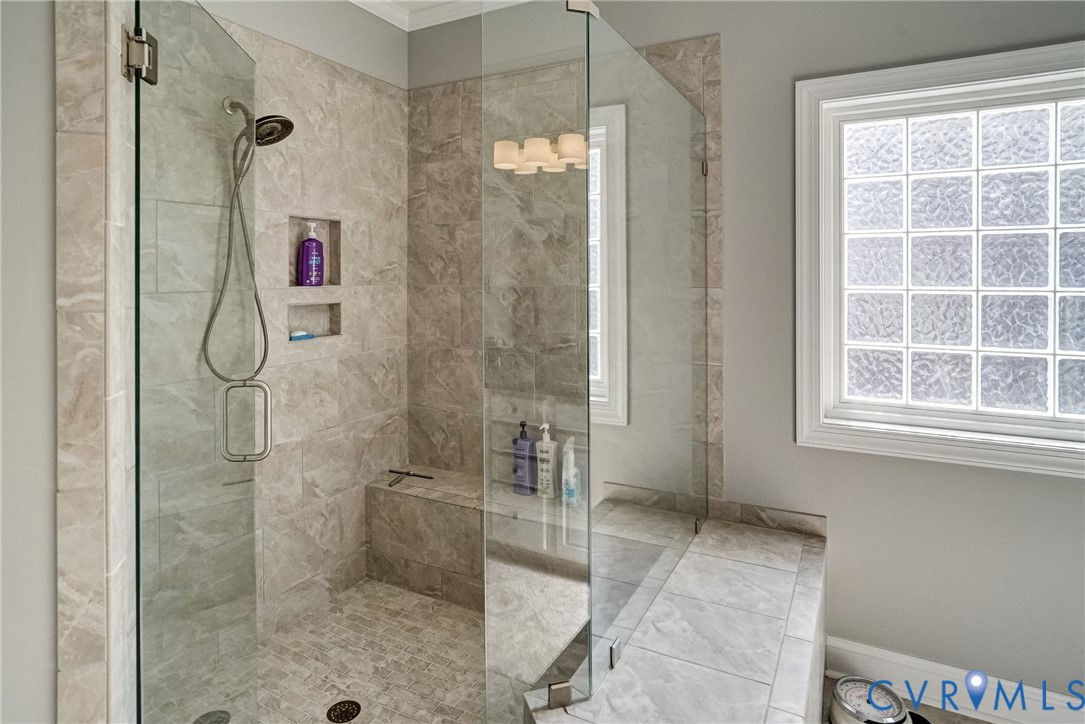 Glass-enclosed shower with stone-look tile walls, a built-in bench, and recessed shelving