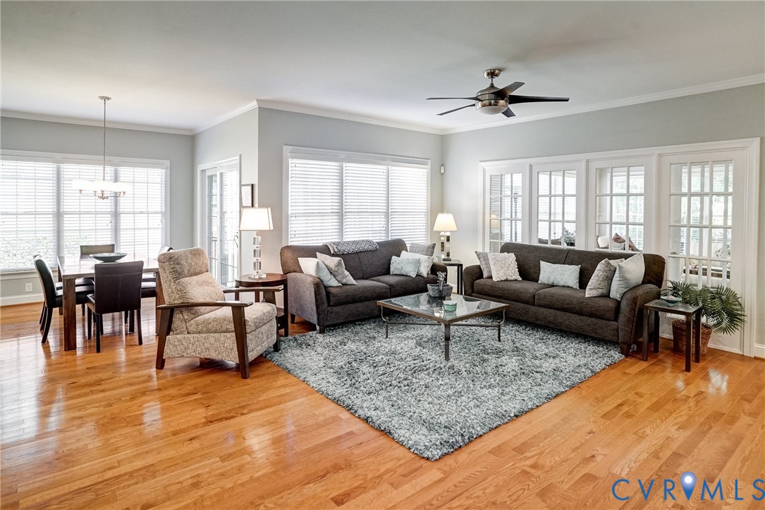 Hardwood flooring throughout, multiple large windows with blinds, a modern ceiling fan, and French doors