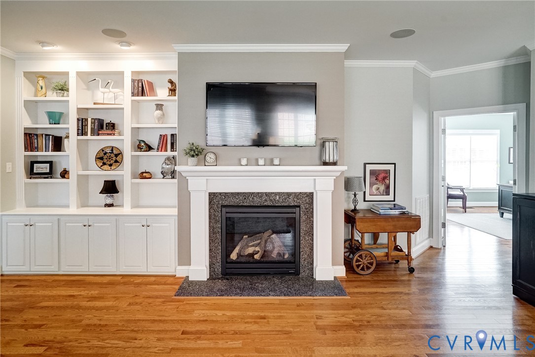 Hardwood flooring complemented by a fireplace featuring a white mantel and dark stone surround