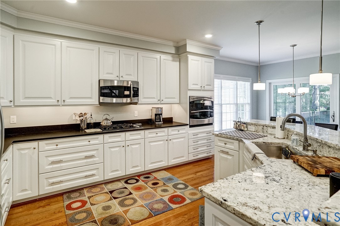 Kitchen featuring white cabinetry, stainless steel appliances, light-toned wood-finish flooring, and light-toned stone countertops