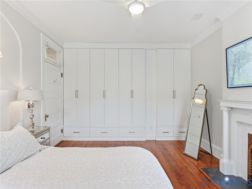 Hardwood flooring, crown molding, built-in cabinetry with integrated drawers, ceiling fan, and decorative fireplace with hearth