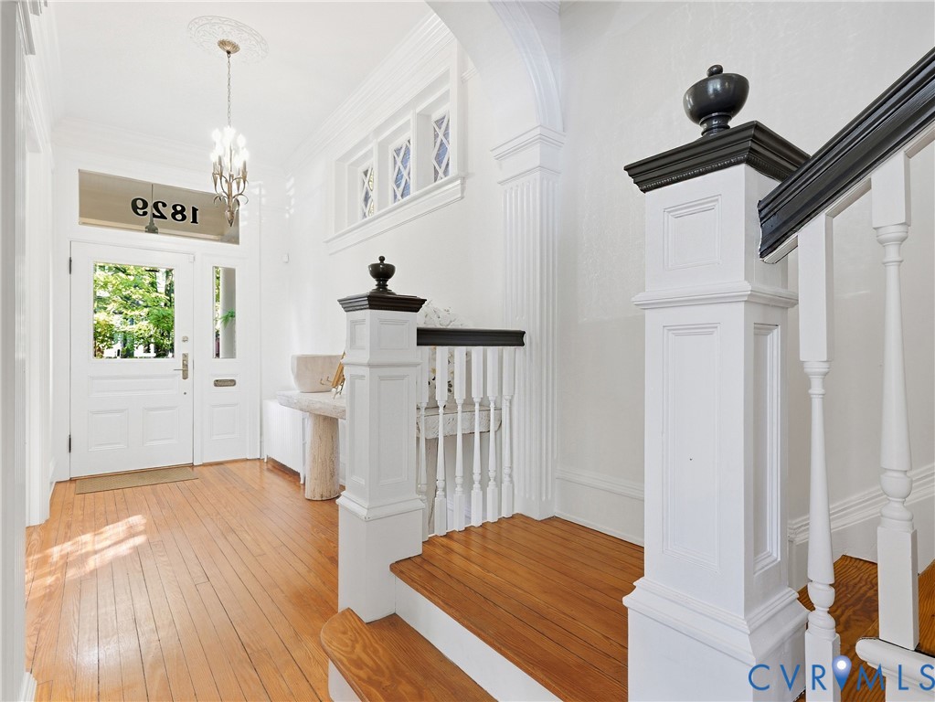 Hardwood flooring, 10+ ft ceilings, white paneled doors, staircase with painted newel posts, decorative archway, and an ornate ceiling medallion