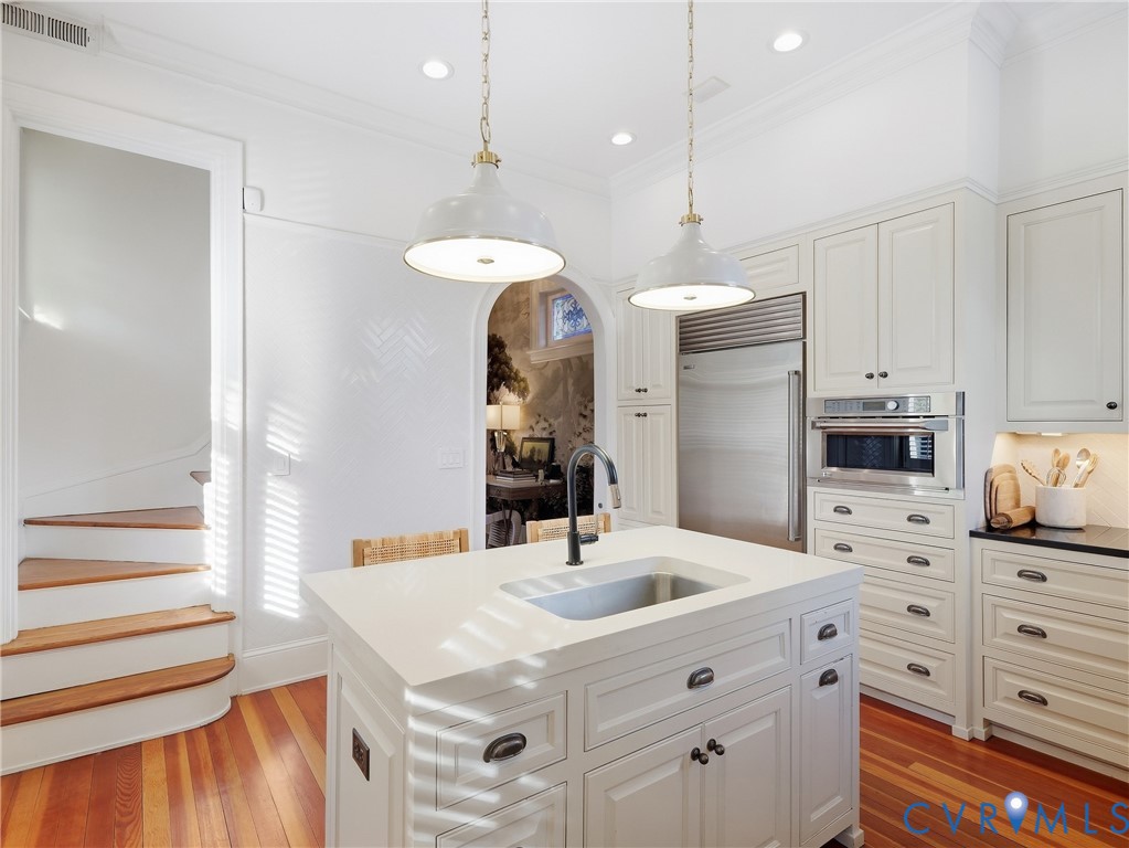 Gourmet kitchen with white cabinetry, built-in stainless steel appliances, a center island with an integrated sink, and pendant lighting