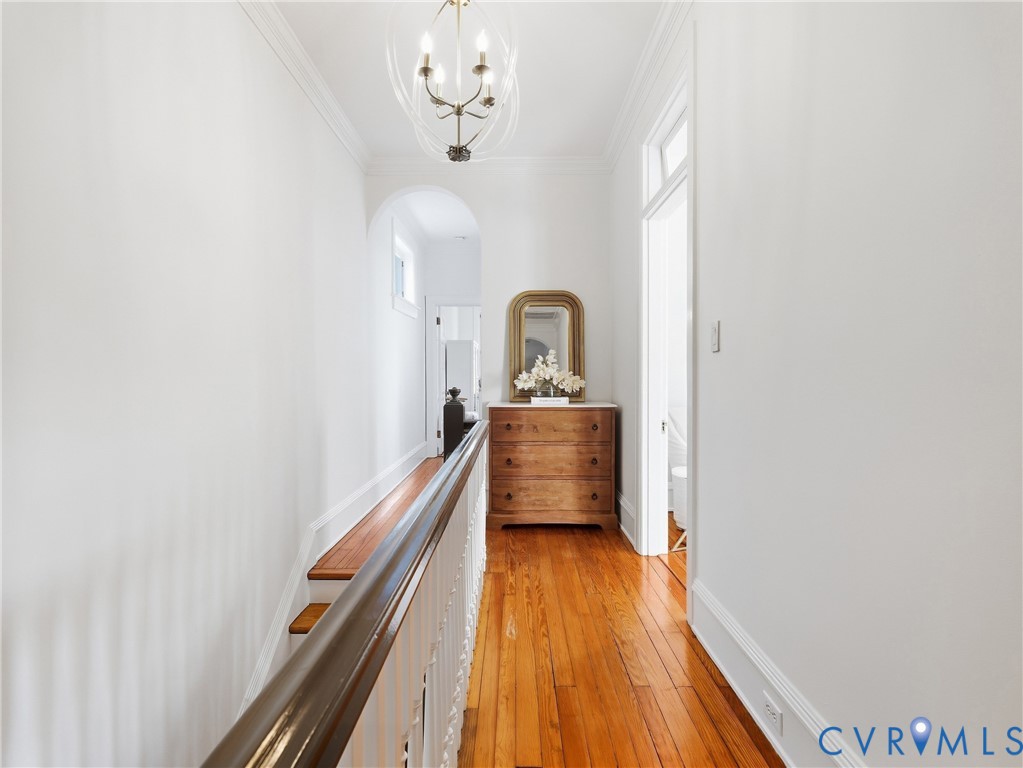 Hardwood flooring, arched doorway, chandelier lighting, crown molding, and white wall finishes