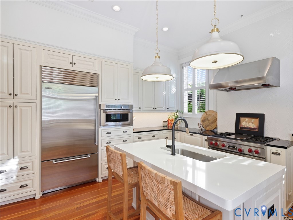 Gourmet kitchen with stainless steel appliances, white cabinetry, a built-in microwave, a gas range with an overhead exhaust hood, and a central island featuring an undermount sink