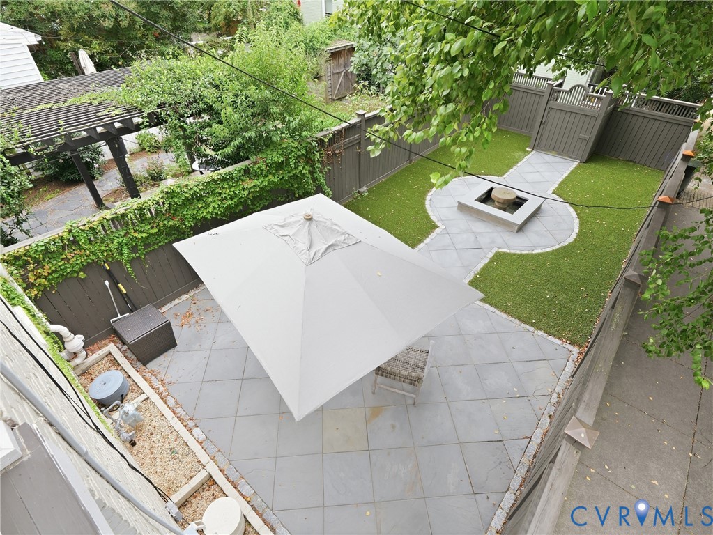 Stone tile patio with a large umbrella, artificial turf, stone fire pit, and privacy fencing