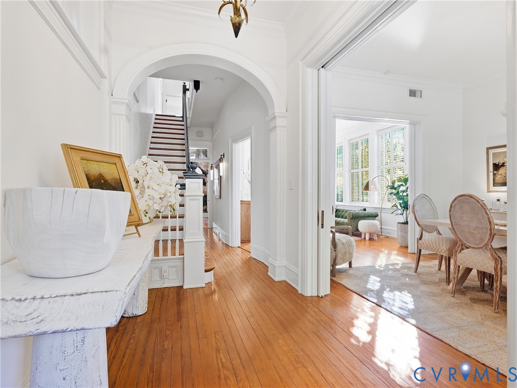 Polished wood-finish flooring, white painted walls, arched entryway, staircase with white newel posts, and interior French doors