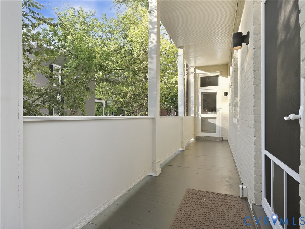 Expansive covered porch featuring painted wood flooring, white painted brick exterior, and a screen door entry