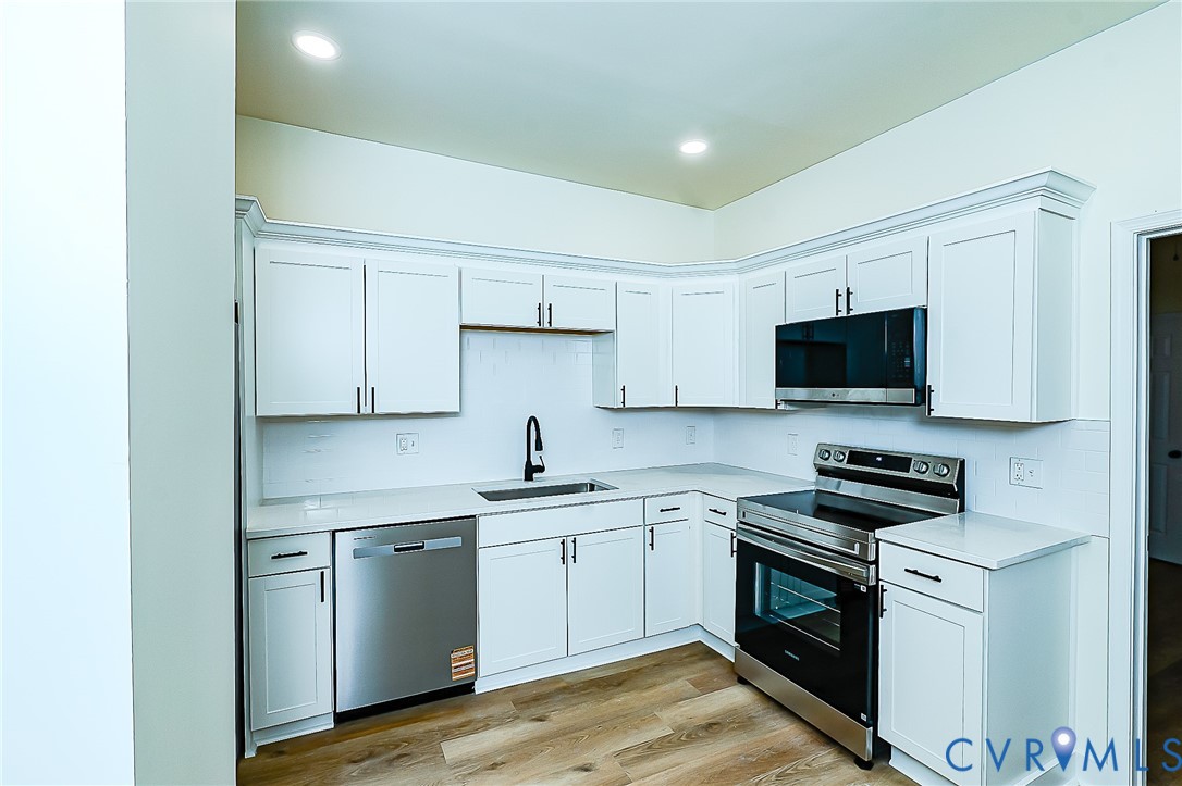 Modern kitchen featuring white shaker cabinetry, stainless steel appliances, a black pull-down faucet, and wood-finish flooring