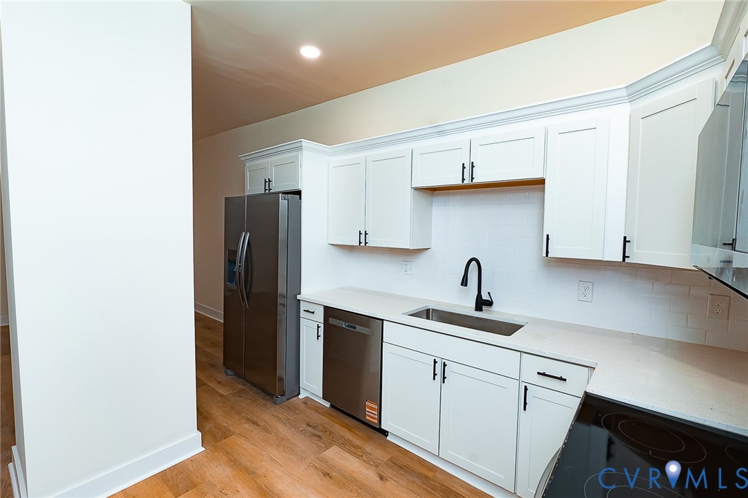 Kitchen featuring white shaker cabinetry, stainless steel appliances, light-toned countertops, subway tile backsplash, and wood-finish flooring
