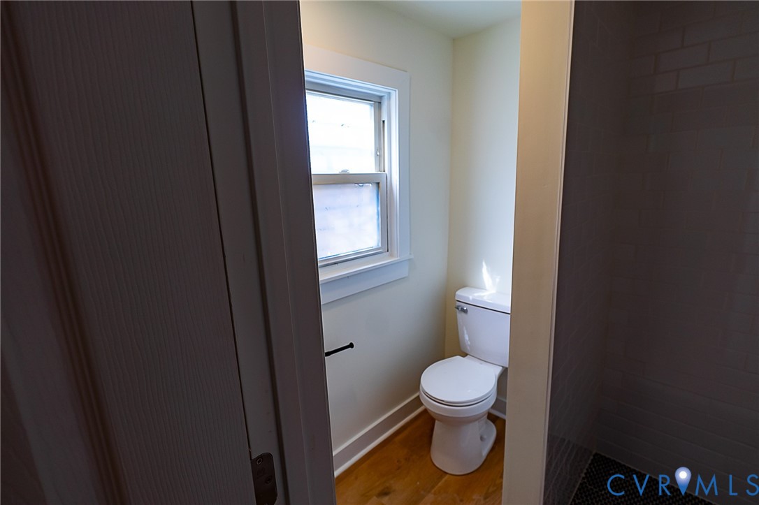 White toilet with a window, LVP flooring, and dark tile wall