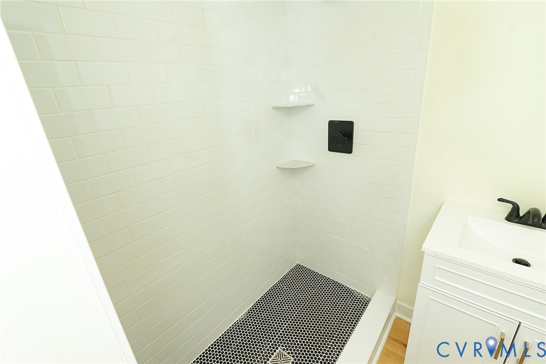Shower stall featuring white subway tile, black penny tile flooring, and integrated corner shelves