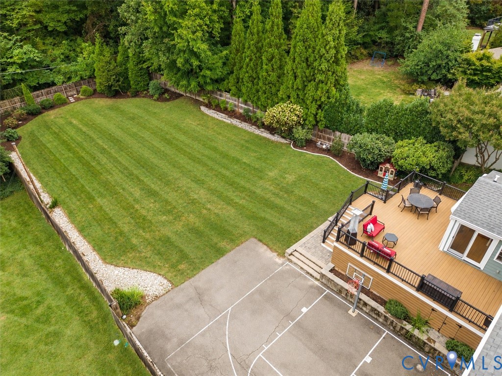 Expansive green lawn framed by mature trees, multi-level composite deck, and paved court with basketball hoop
