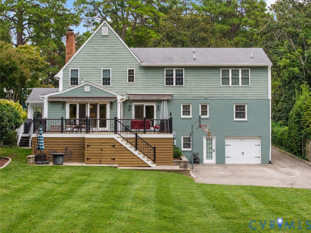 Expansive rear lawn, multi-level composite deck with black railings, walk-out basement with integrated garage, and a brick chimney accent