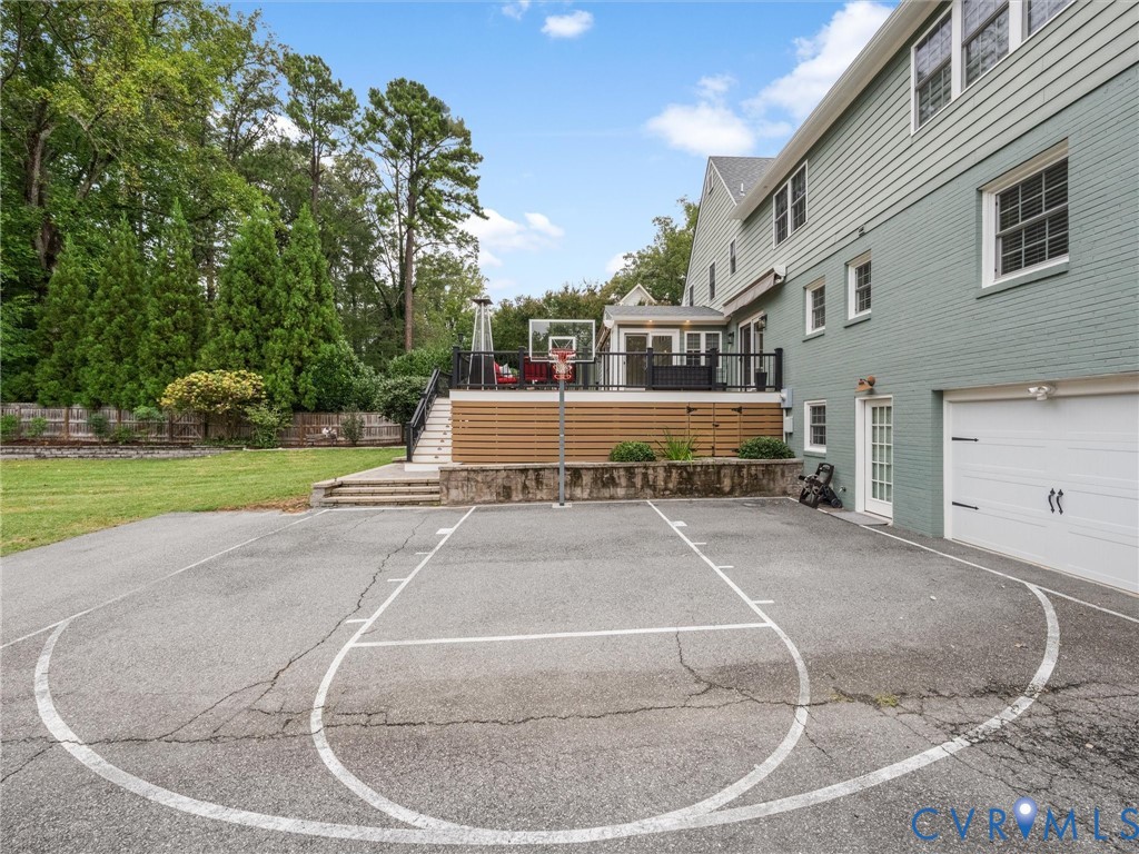 Backyard featuring a dedicated sports court, multi-level composite deck with black railings, and a two-car garage