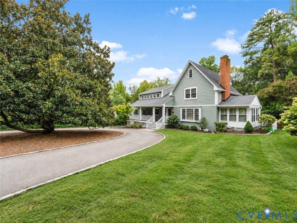 Expansive front lawn with mature landscaping, a paved driveway, and a covered porch