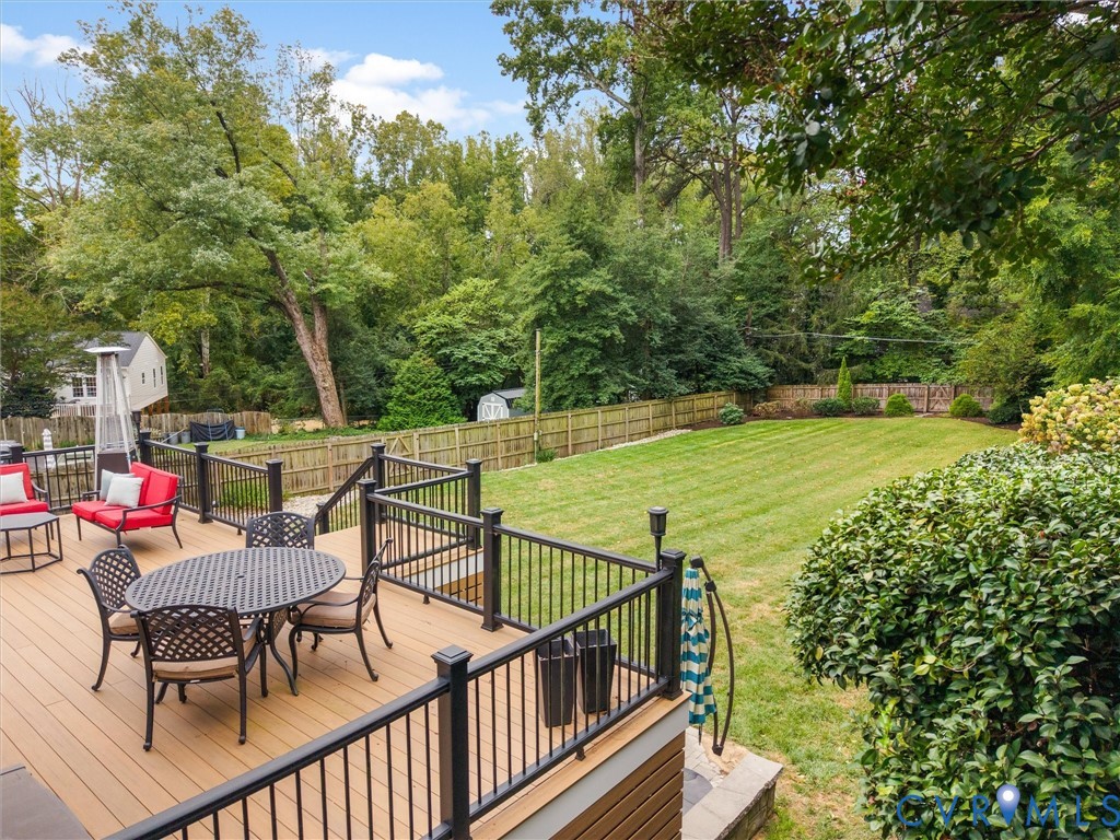 Expansive backyard featuring a large green lawn, wood-toned decking, and black railings
