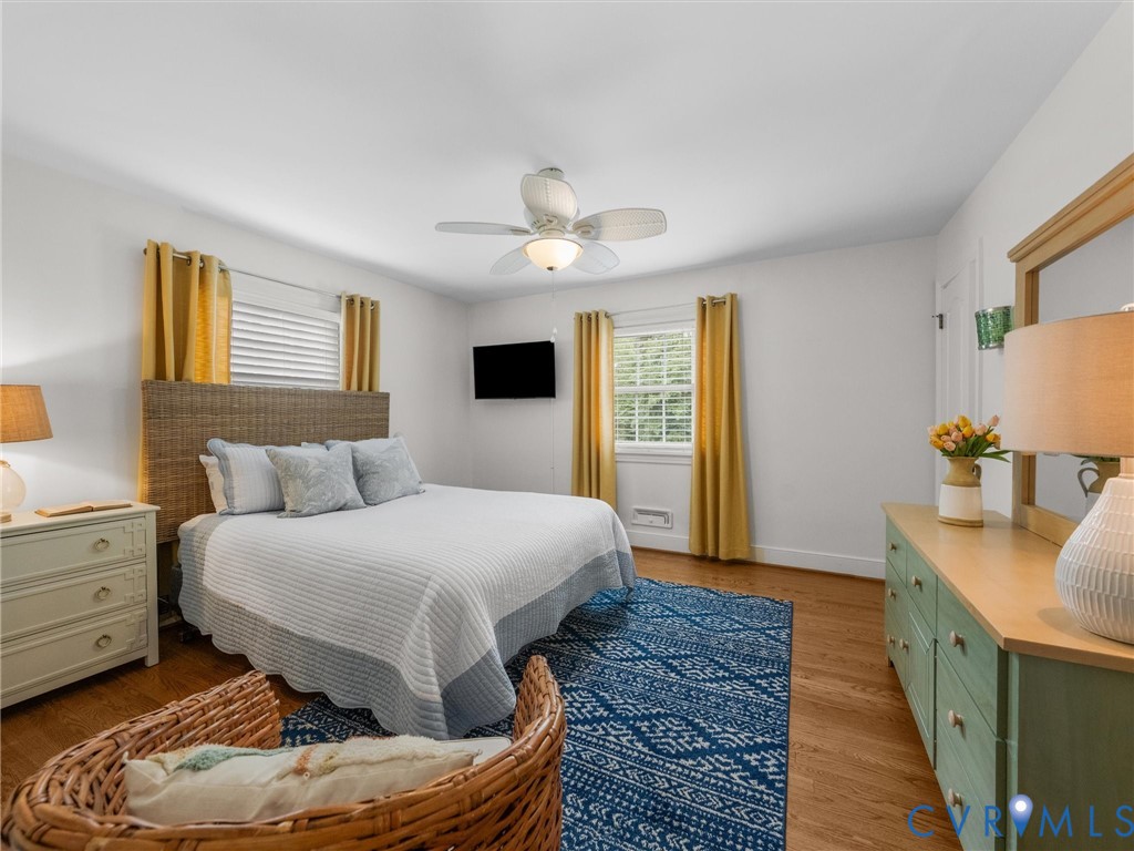 Wood-finish flooring, ceiling fan with integrated lighting, and multiple windows with horizontal blinds