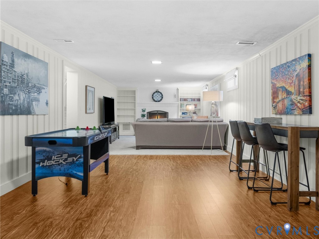 Expansive room featuring wood-finish flooring, white paneled walls, recessed lighting, and a built-in fireplace with white mantel and shelving