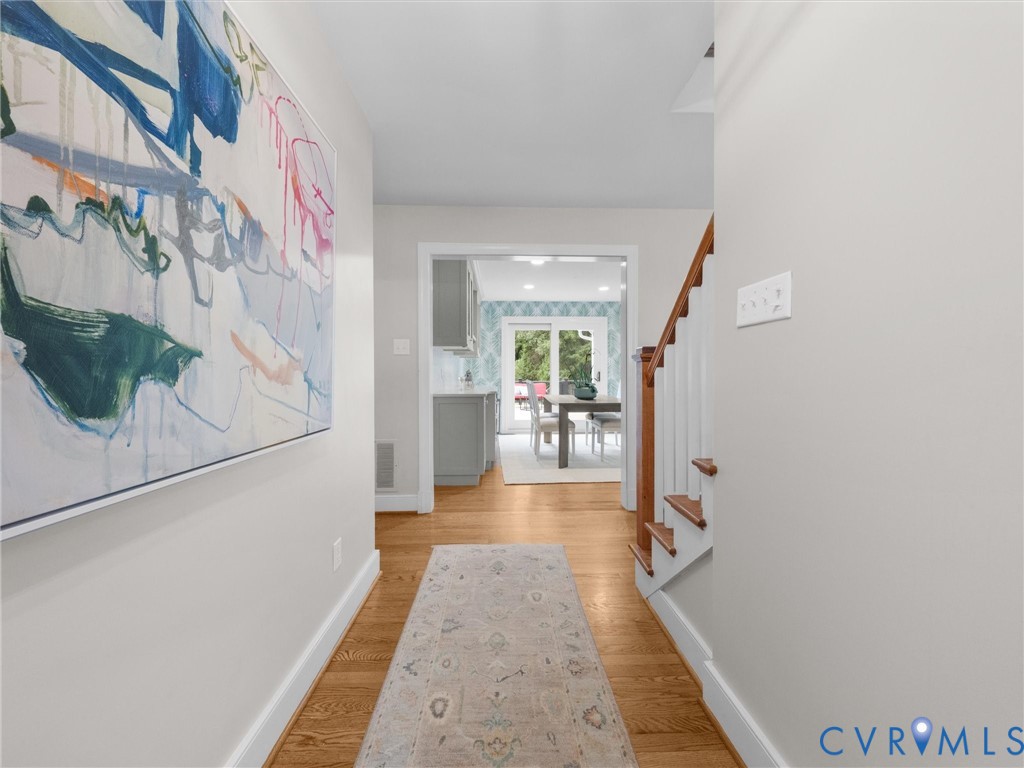 Hardwood flooring, painted interior walls, wood staircase with white risers, doorway leading to an additional space, and a kitchen with grey cabinetry