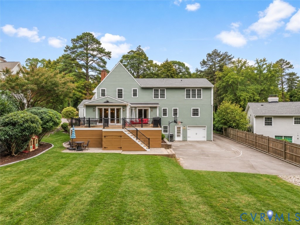 Expansive green lawn with mature landscaping, multi-level deck, direct garage access, and a paved driveway