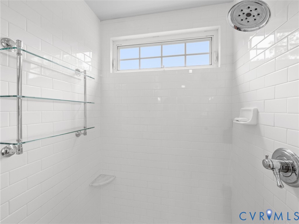 Shower with white subway tile, a chrome shower head, a chrome shower control, three glass shelves, and a transom window