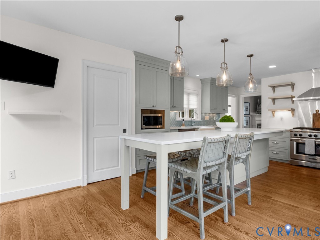 Kitchen featuring wood-finish flooring, an expansive island with countertop seating, three pendant lights, custom cabinetry, and stainless steel appliances