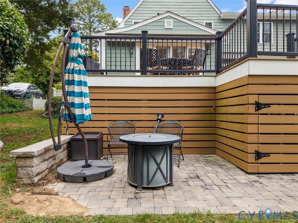 Paved patio area, stone retaining wall, composite deck with black railings, horizontal wood-look siding, and integrated storage with black hardware