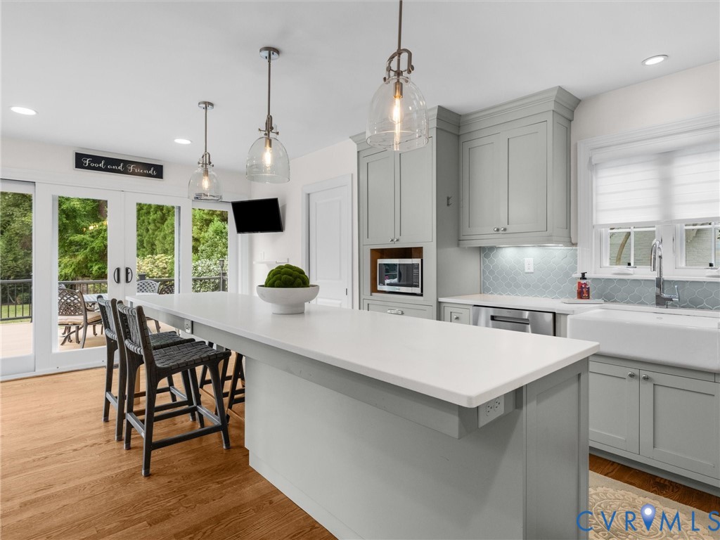 Expansive kitchen island with seating, pendant lighting, light gray cabinetry, and white countertops